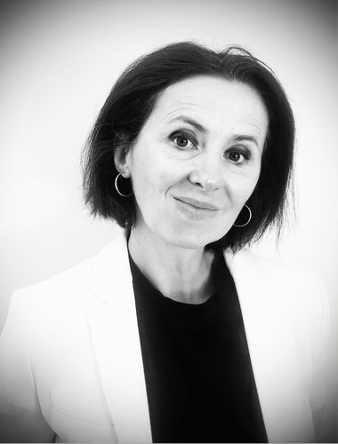 Une femme portant des lunettes et une veste noire sourit sur une photo en noir et blanc.