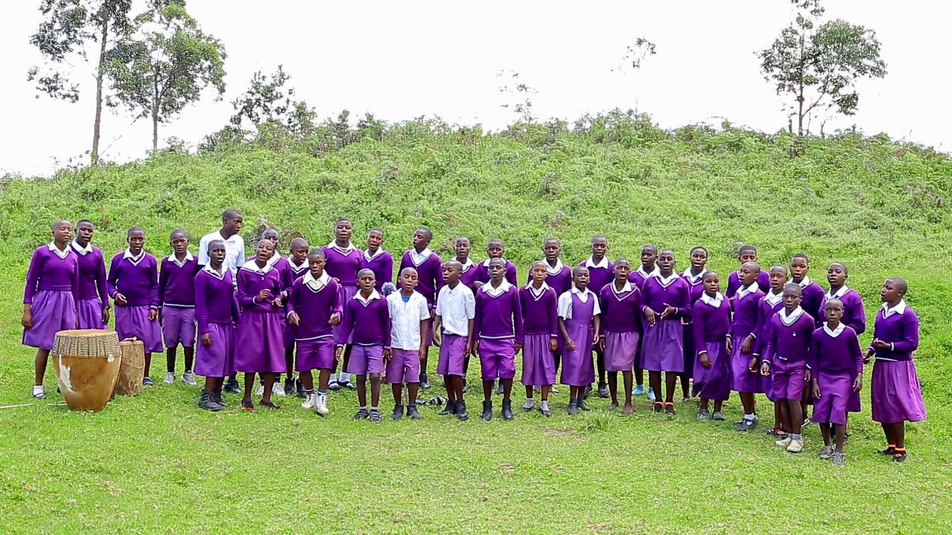 A large group of children in purple uniforms are standing in a grassy field.