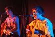 Two men are singing into microphones while playing guitars