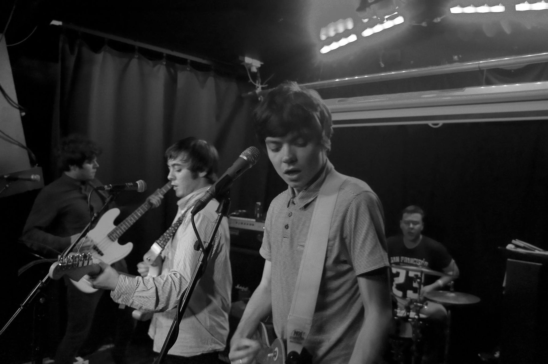 A group of young men are playing guitars and singing into microphones on a stage.