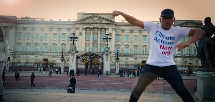 A man wearing a climate action now shirt is standing in front of a large building.