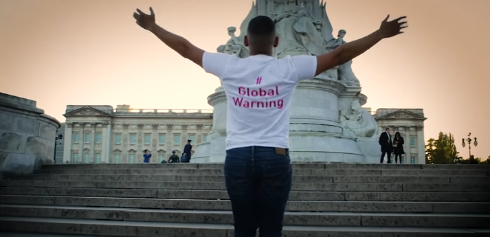 A man wearing a global warning t-shirt is standing in front of a statue.