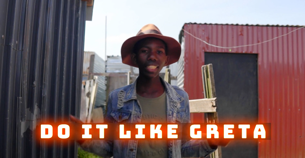 A man wearing a hat and a denim jacket is standing in front of a red building.