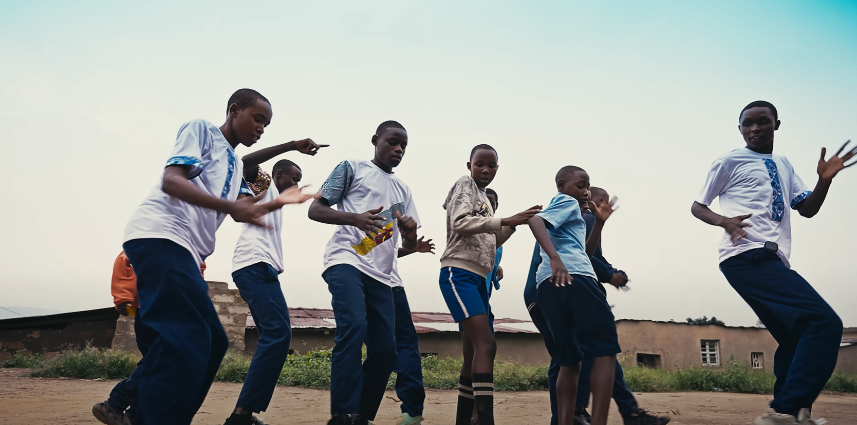 A group of young boys are dancing in a dirt field.