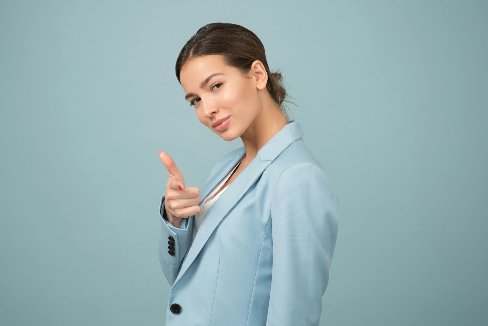 A woman in a blue suit is pointing at the camera.