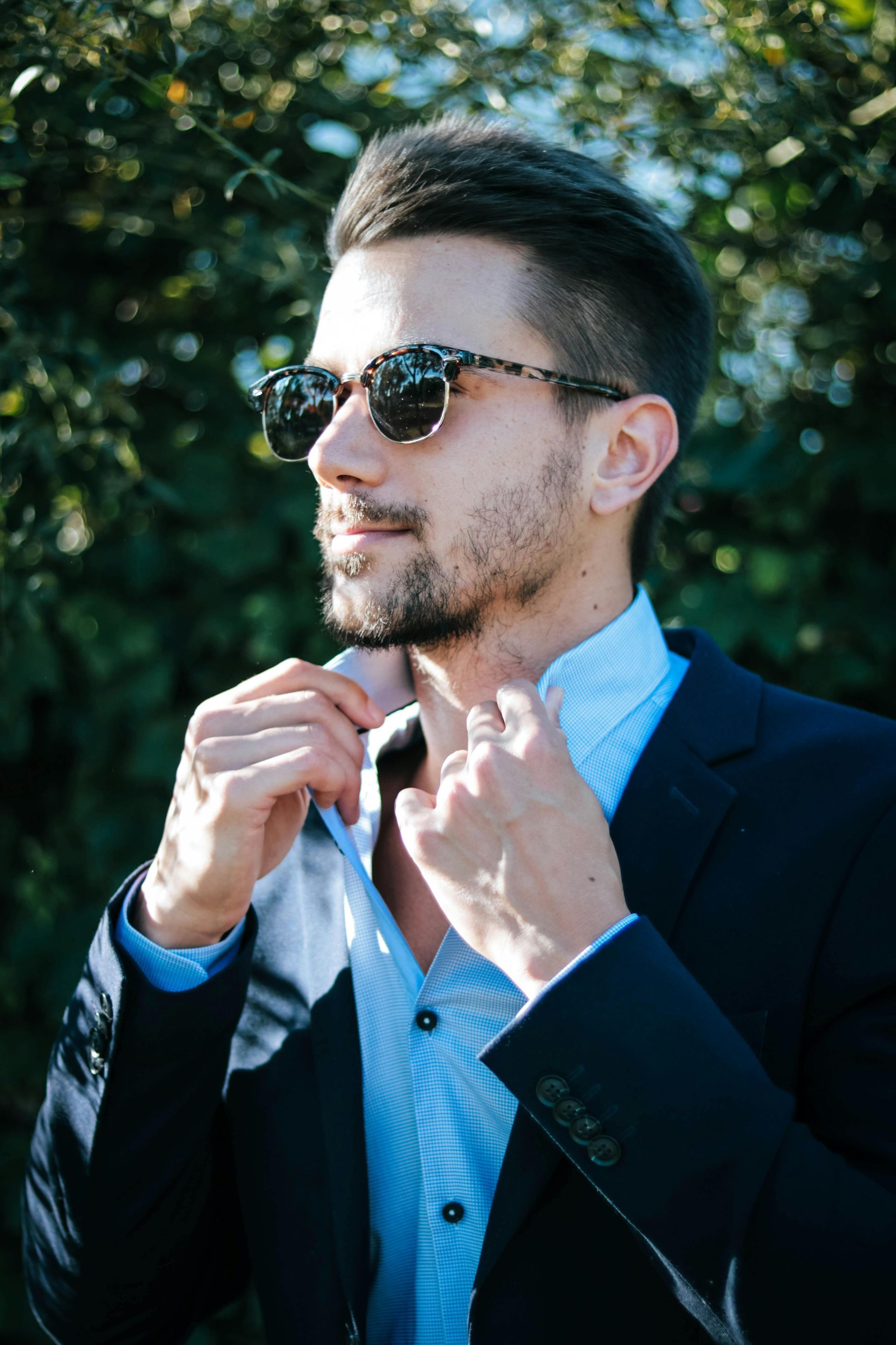 A man in a suit and sunglasses is adjusting his tie.
