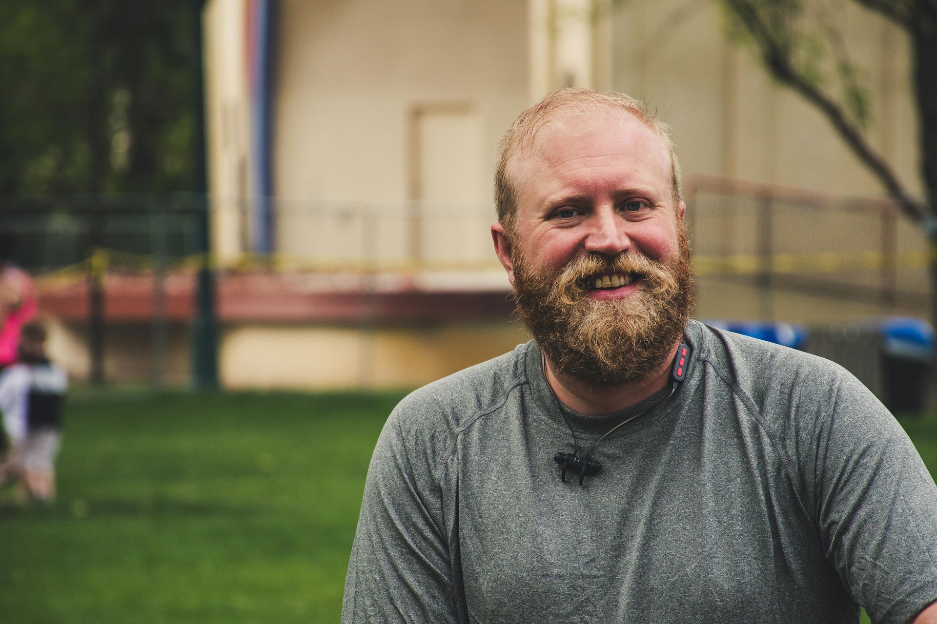 A man with a beard is smiling for the camera in a park.
