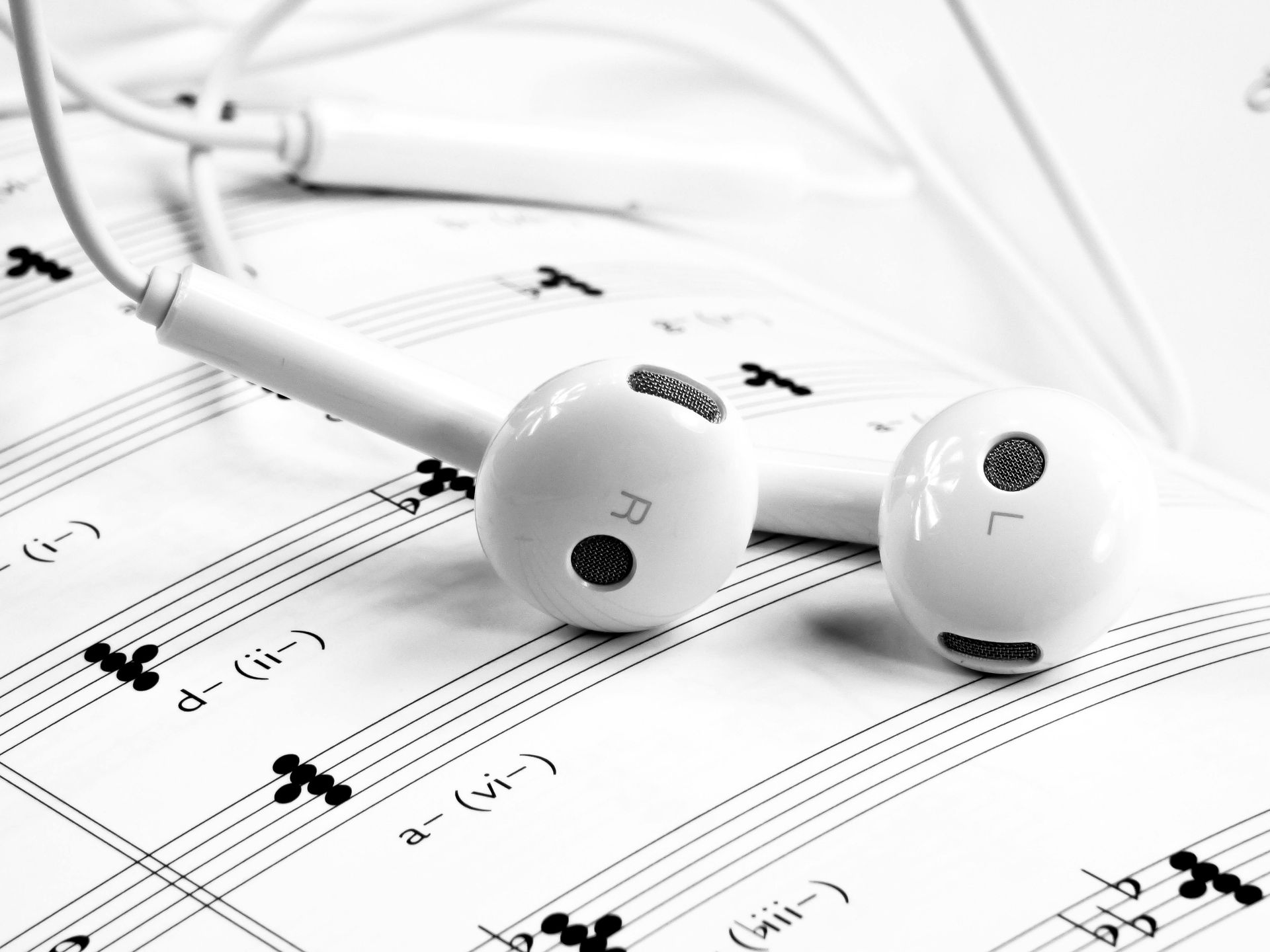 A pair of white ear buds laying on top of a sheet of music