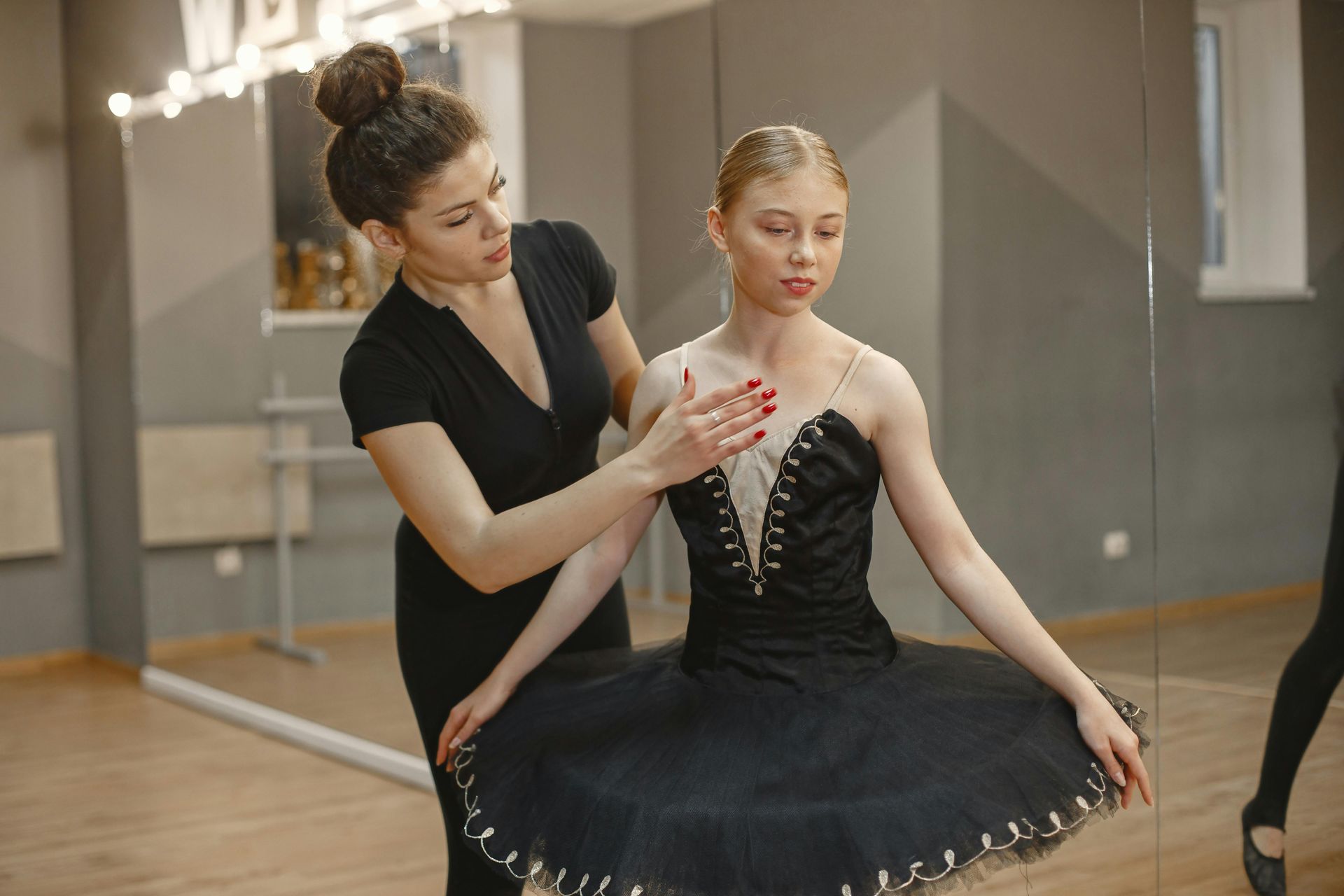 A woman is helping a ballerina with her dress in a dance studio.