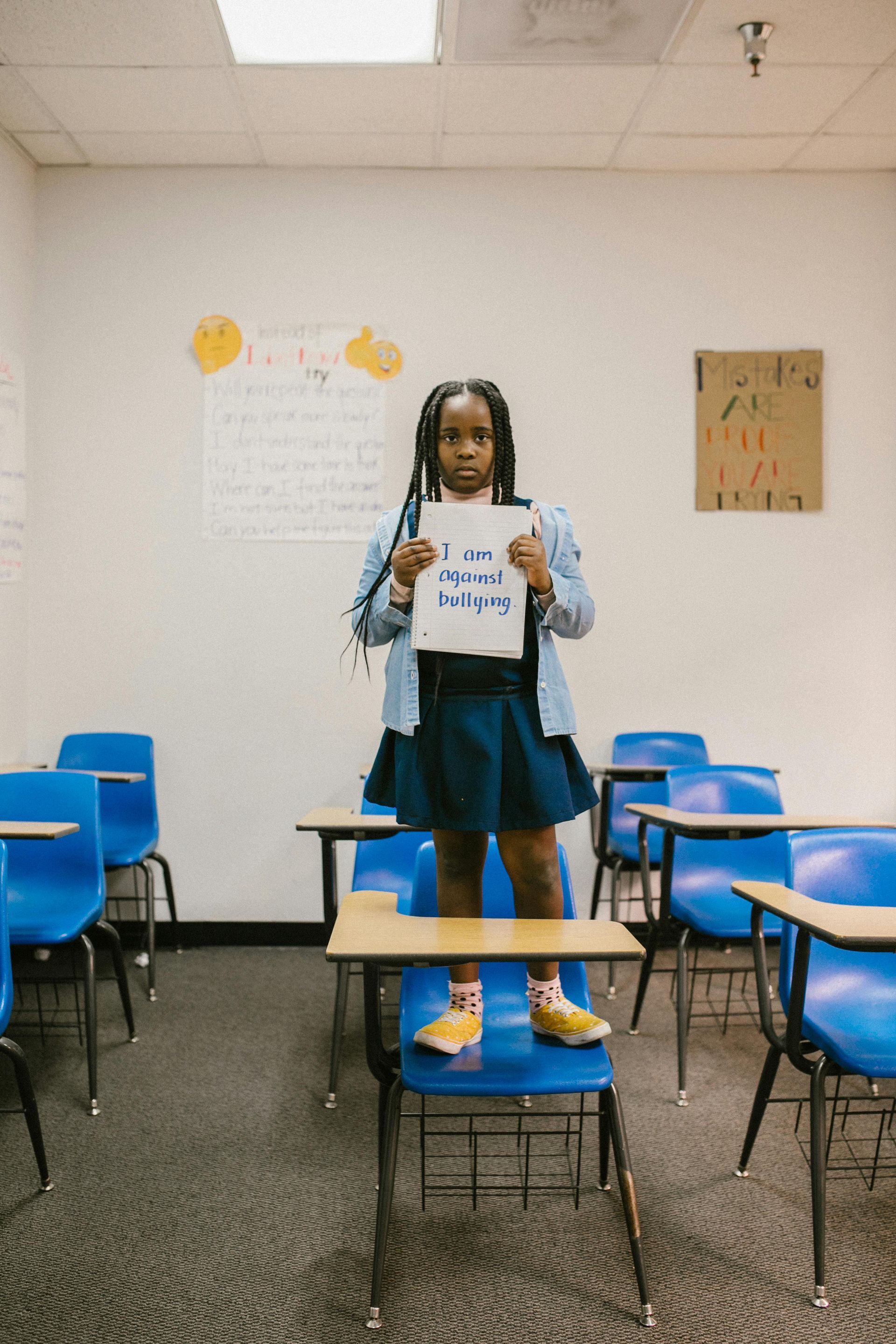 A young girl is standing in a classroom holding a sign.