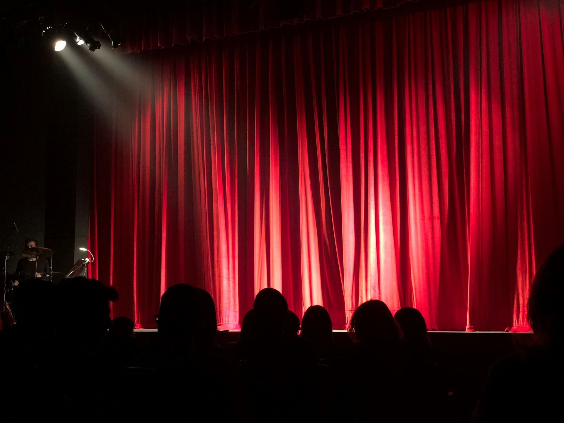 A group of people sitting in front of a stage with red curtains
