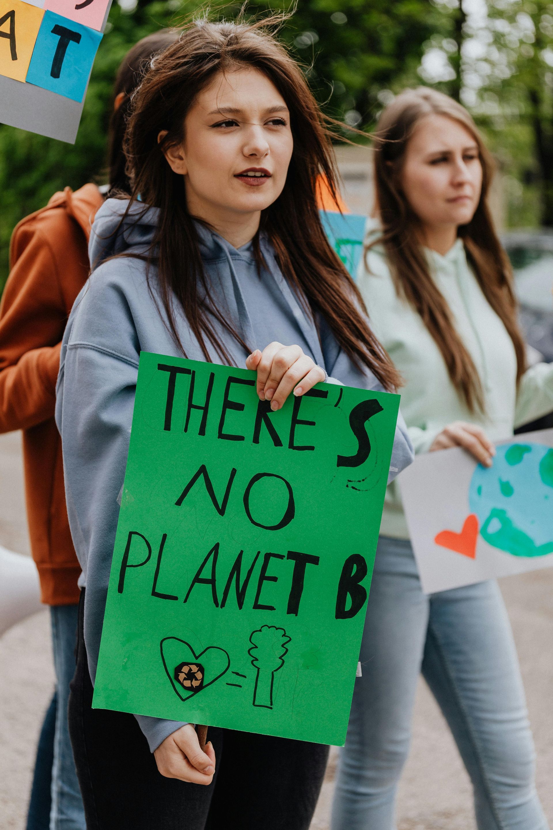 A woman is holding a green sign that says `` there 's no planet b ''.