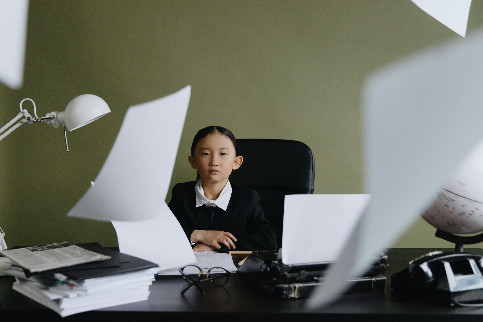 A little girl is sitting at a desk with papers flying around her.