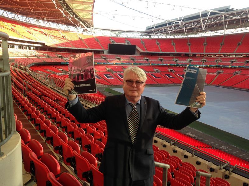 A man in a suit and tie is holding two books in a stadium