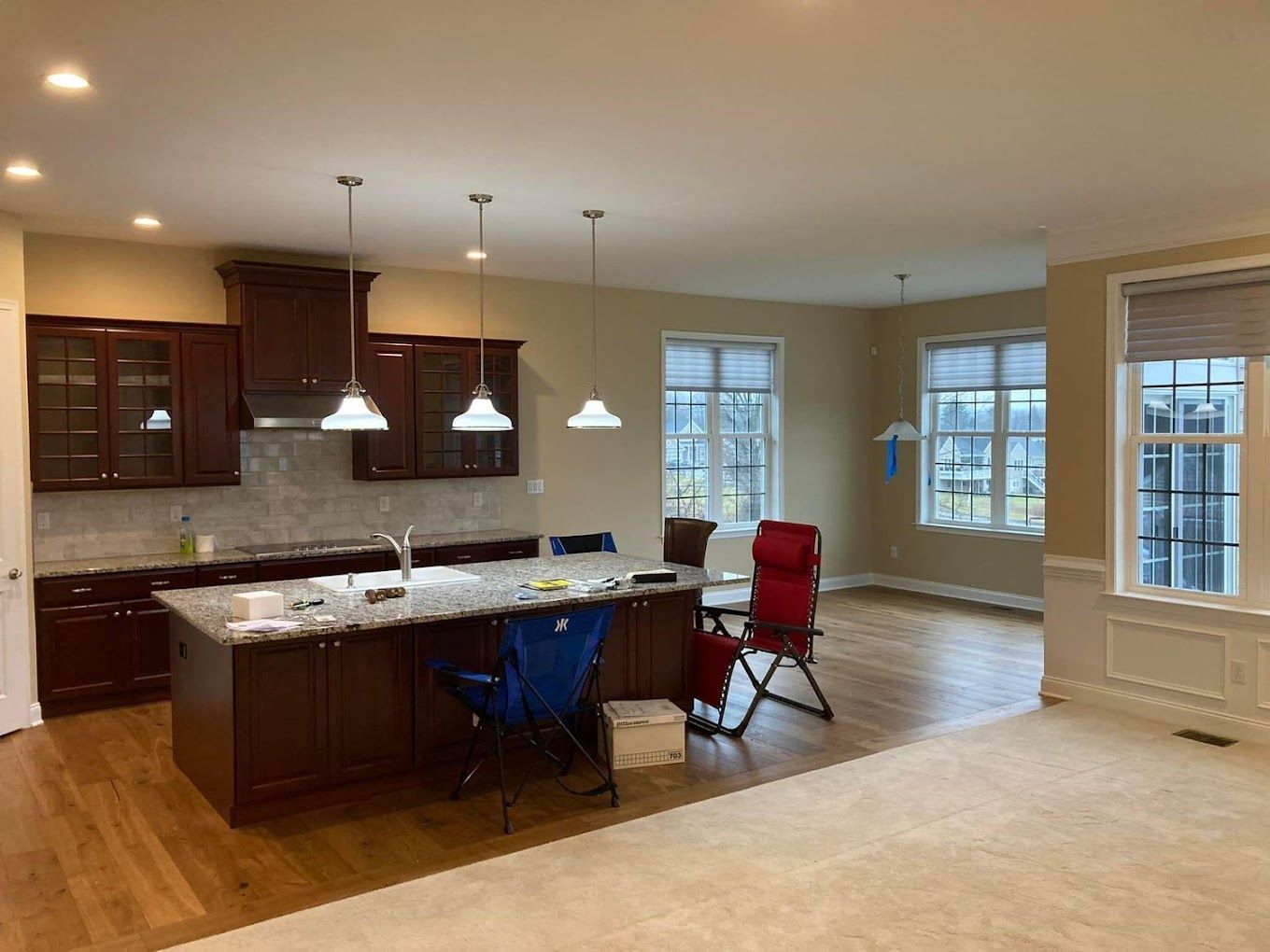 Open kitchen with brown cabinets, island, and wooden floors; windows in the background.