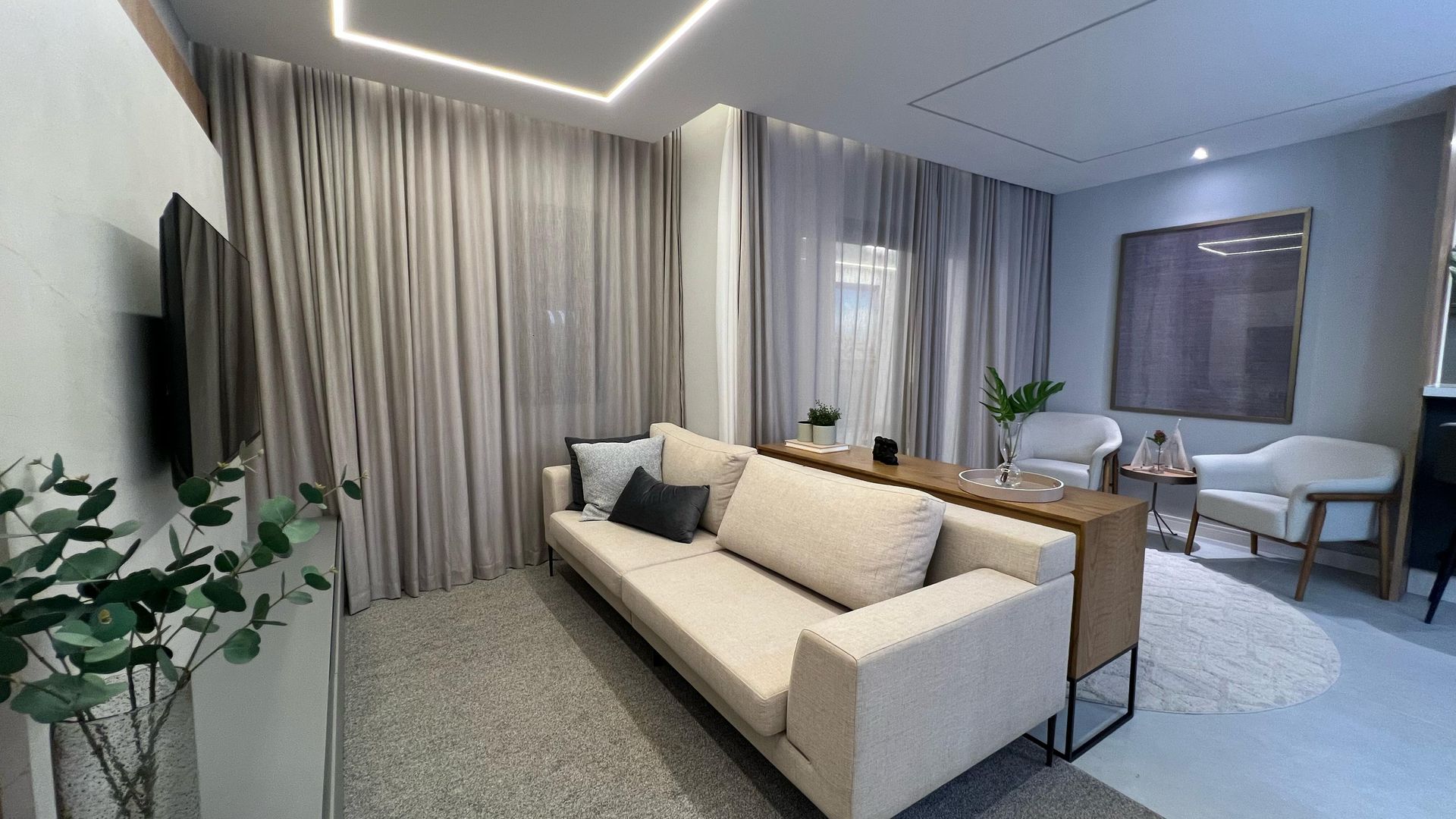 Sala de estar aconchegante com sofá bege, cortinas cinza e um tapete branco felpudo.