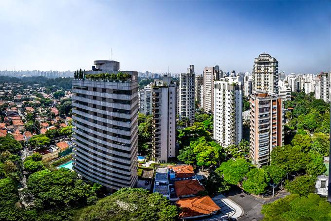 Vista da cidade com prédios altos, árvores verdes e céu azul.