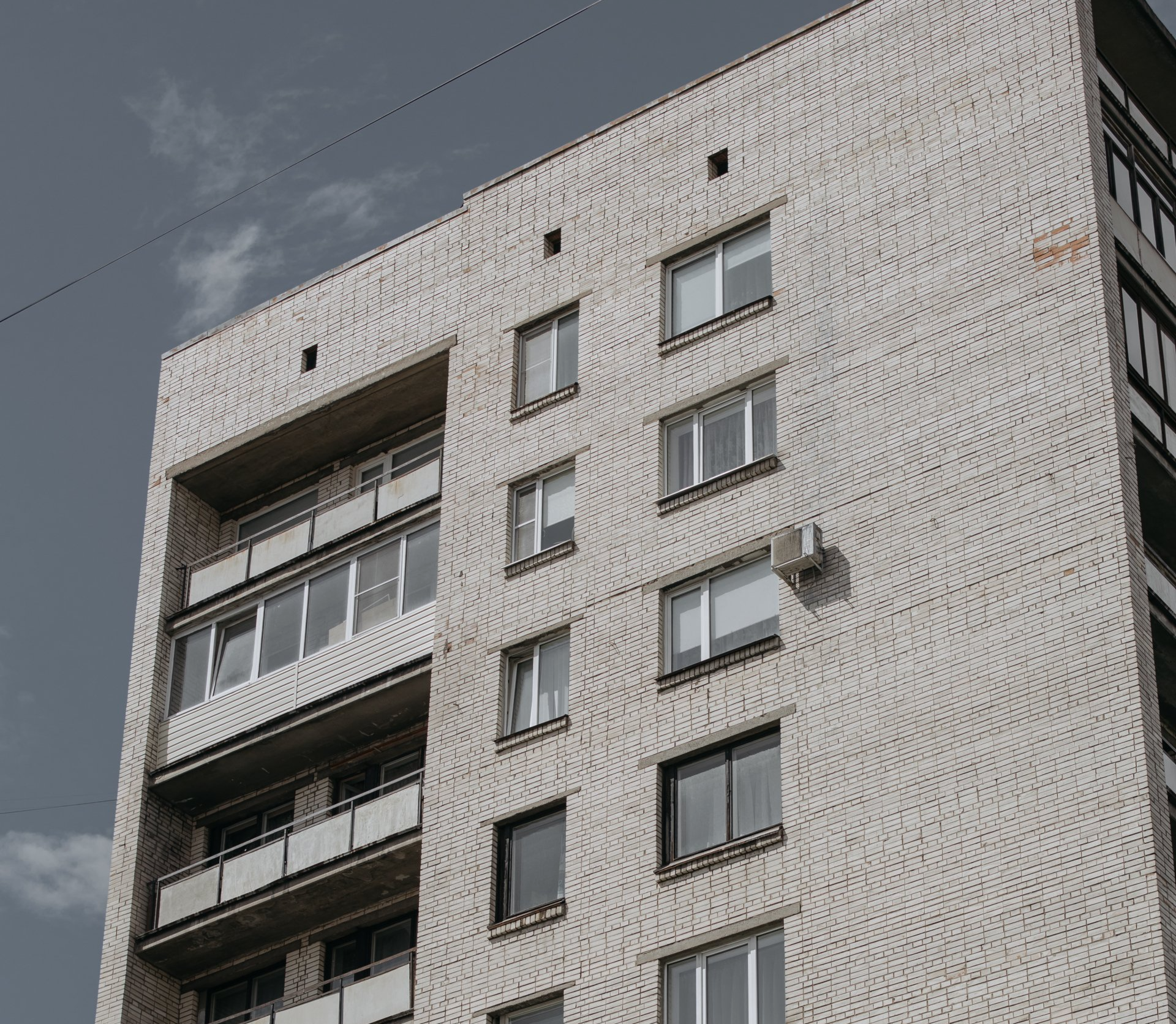 Prédio de tijolos com vários andares, varandas e janelas retangulares, sob um céu nublado.