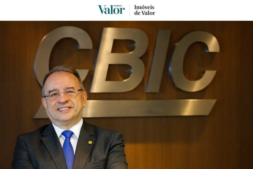 Homem de terno sorrindo em frente ao logotipo 