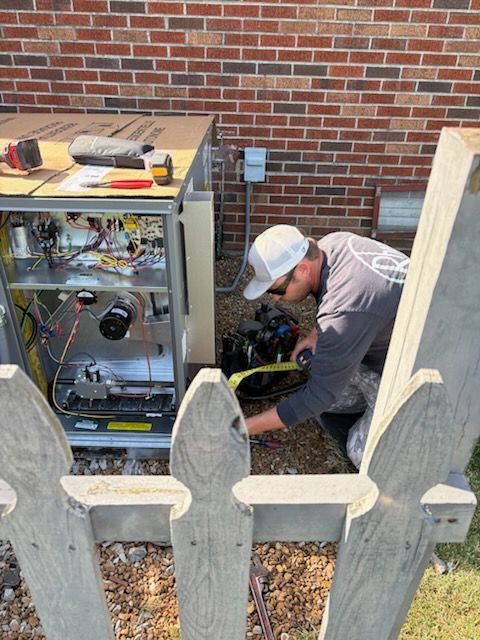 A man is working on an air conditioner outside of a brick building.