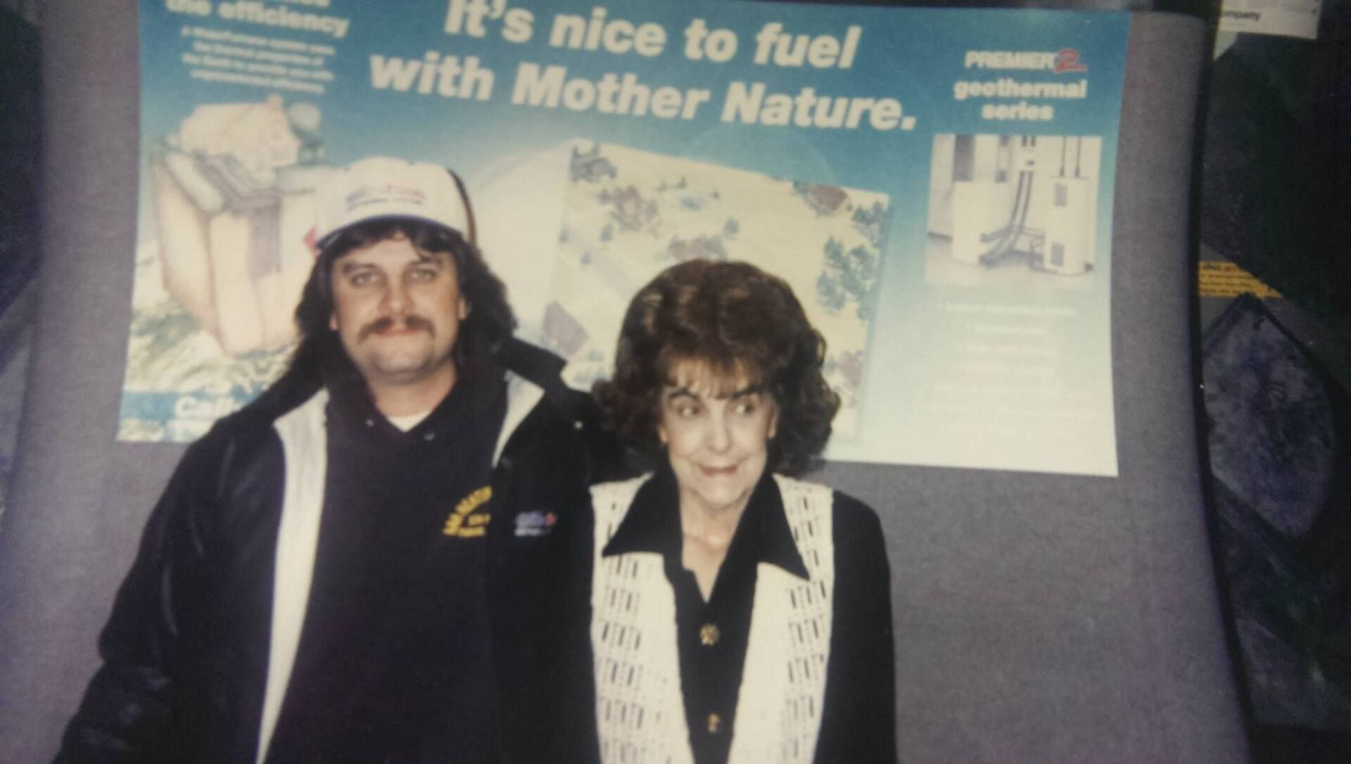 A man and a woman standing in front of a poster that says it 's nice to fuel with mother nature