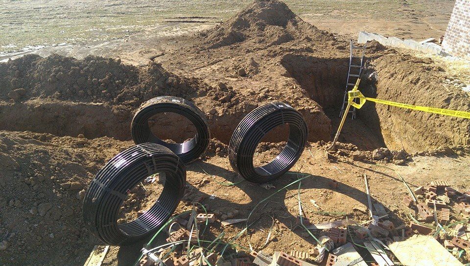Three tires are sitting in the dirt near a hole in the ground.