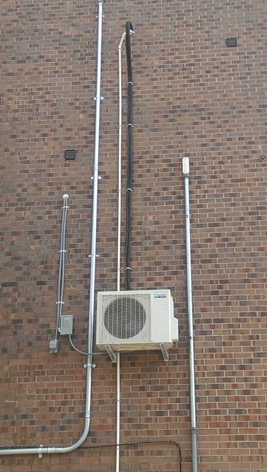 A white air conditioner is mounted on the side of a brick building.