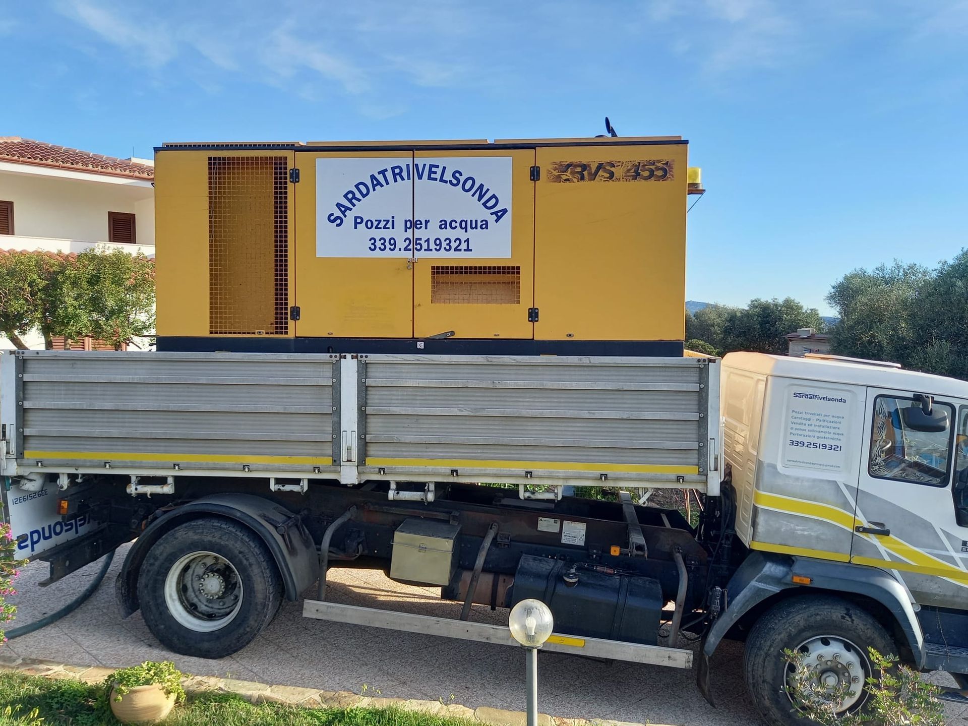 Generatore giallo sul cassone di un camion con testo, sullo sfondo cielo e un edificio Sarda Trivelsonda Group Olbia  Loiri Porto San Paolo - Loiri (SS)