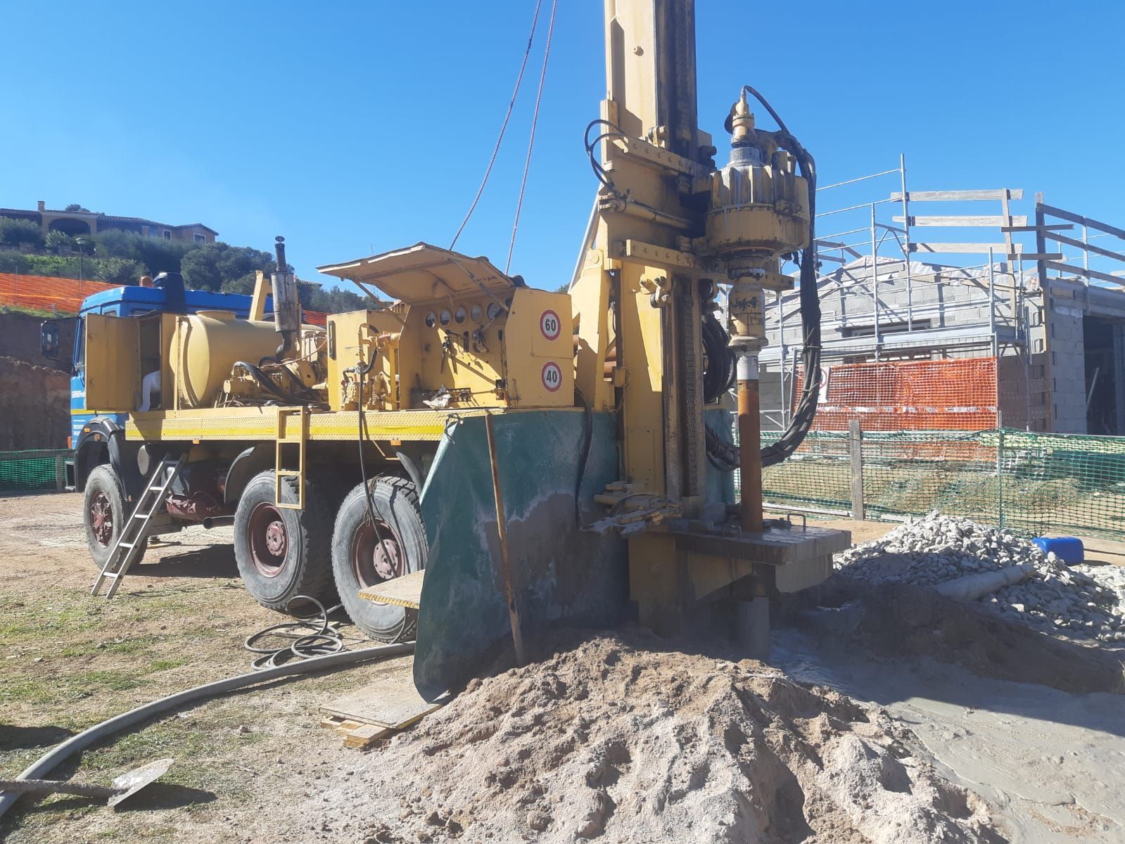 Una piattaforma di perforazione gialla in un cantiere edile, vicino a un cumulo di terra. Il cielo è azzurro e luminoso Sarda Trivelsonda Group Olbia  Loiri Porto San Paolo - Loiri (SS)