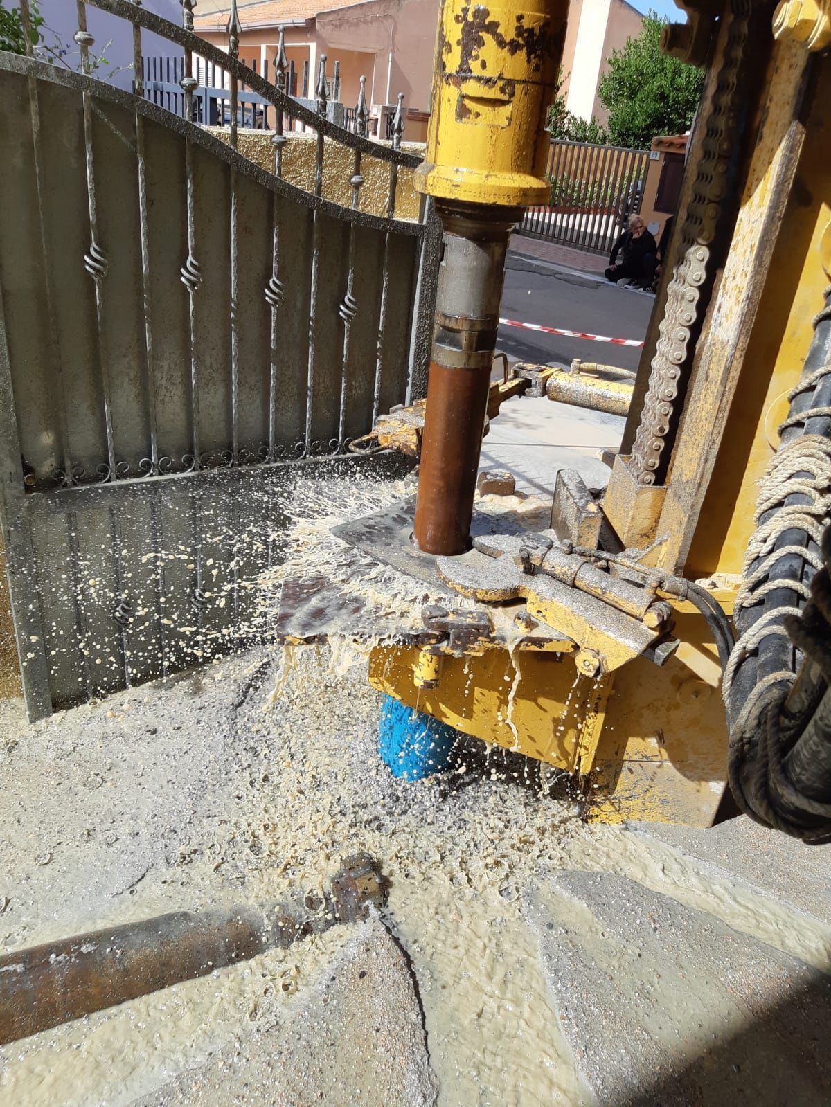 Macchina edile gialla che perfora il cemento vicino a un cancello metallico, producendo polvere Sarda Trivelsonda Group Olbia  Loiri Porto San Paolo - Loiri (SS)