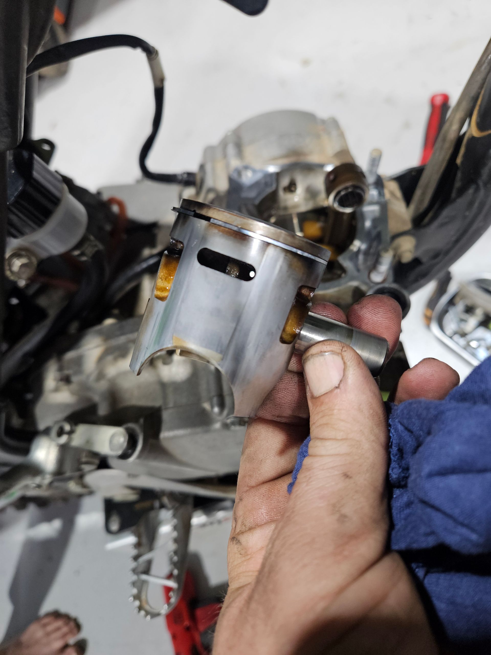 Hand Holding a Silver Engine Piston Near a Motorcycle — Cap Coast Maintenance In Alton Downs, QLD