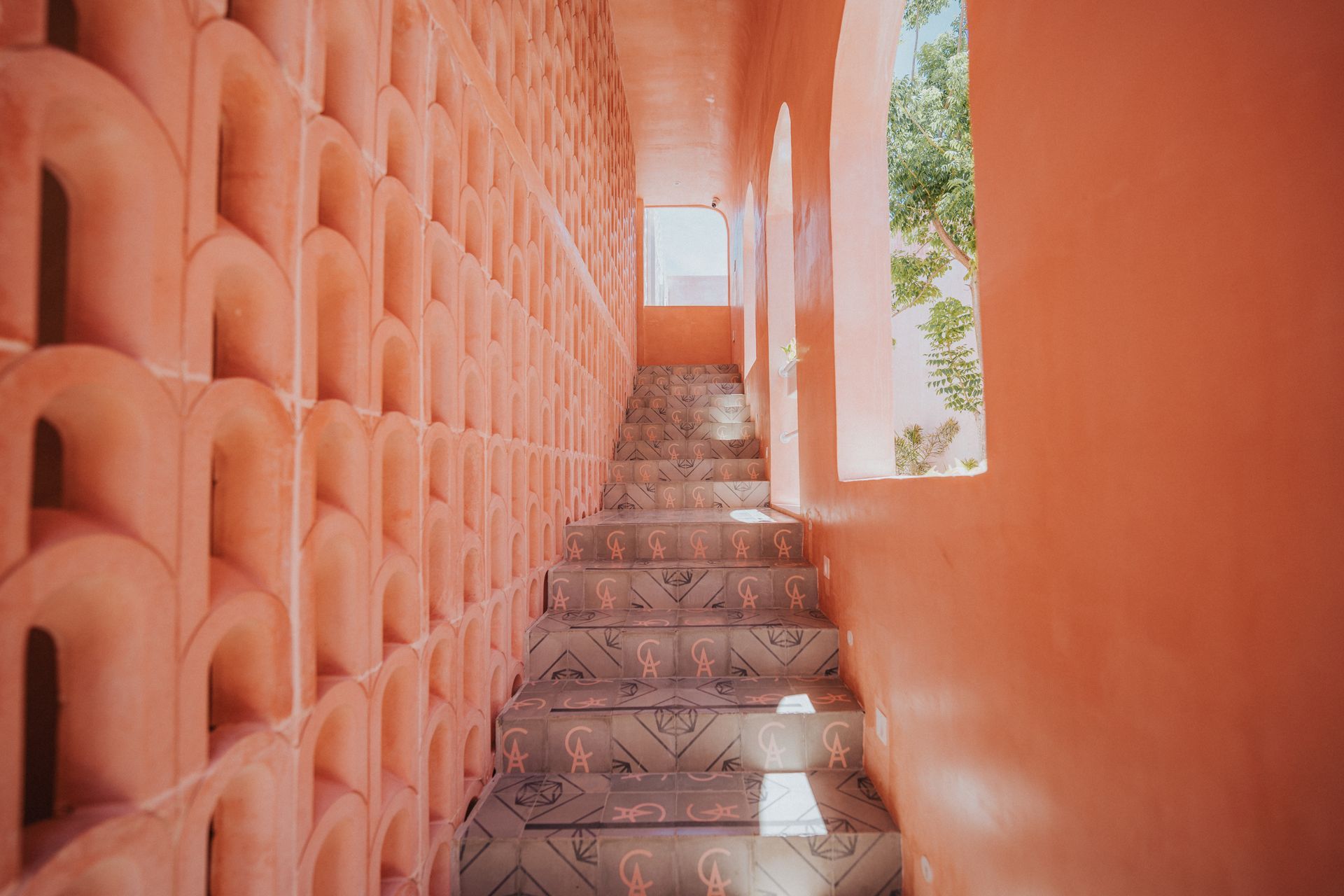 Un pasillo con escaleras que conducen a una ventana y una pared rosa.