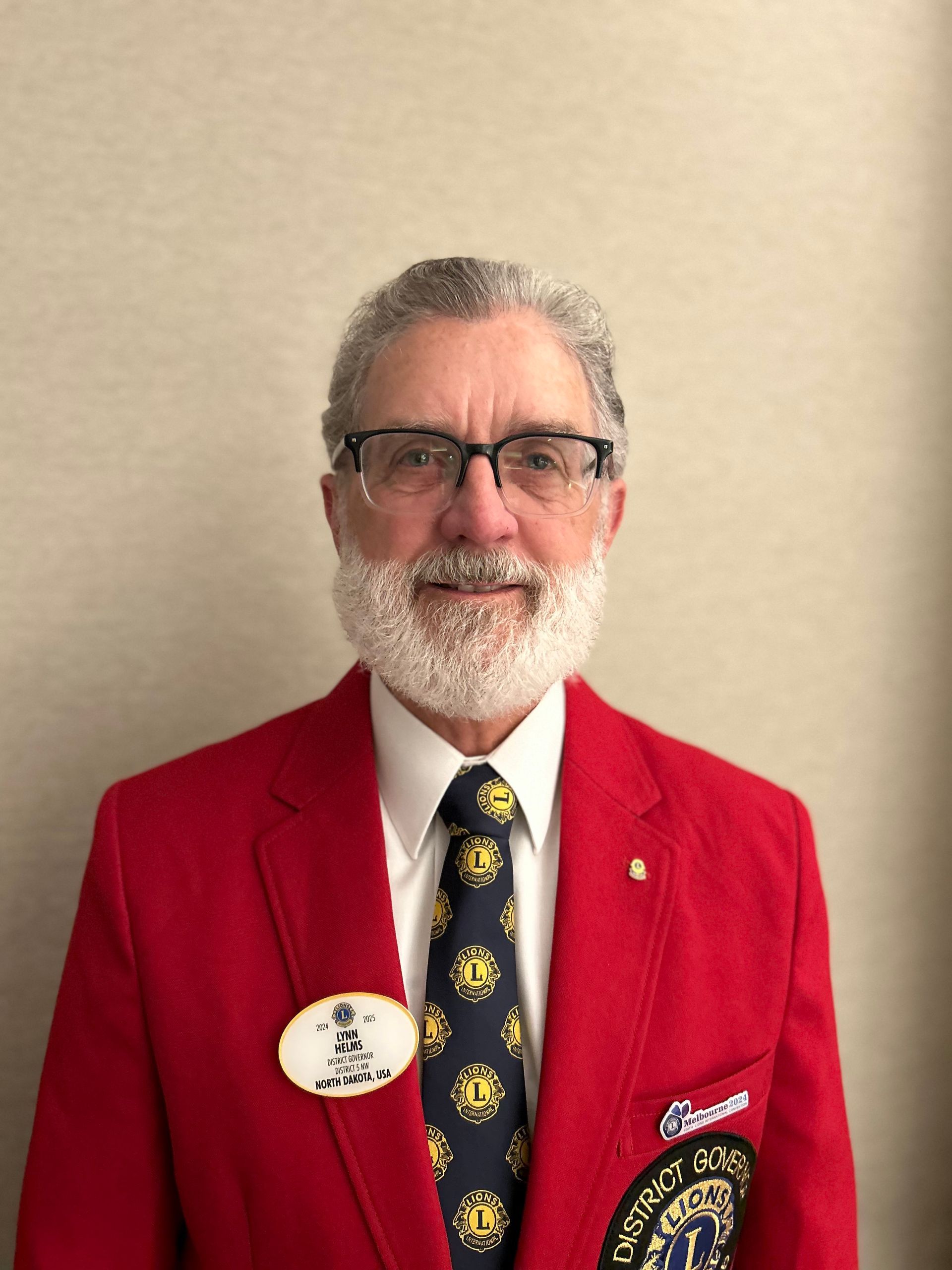 A man with a beard and glasses is wearing a red jacket and tie.