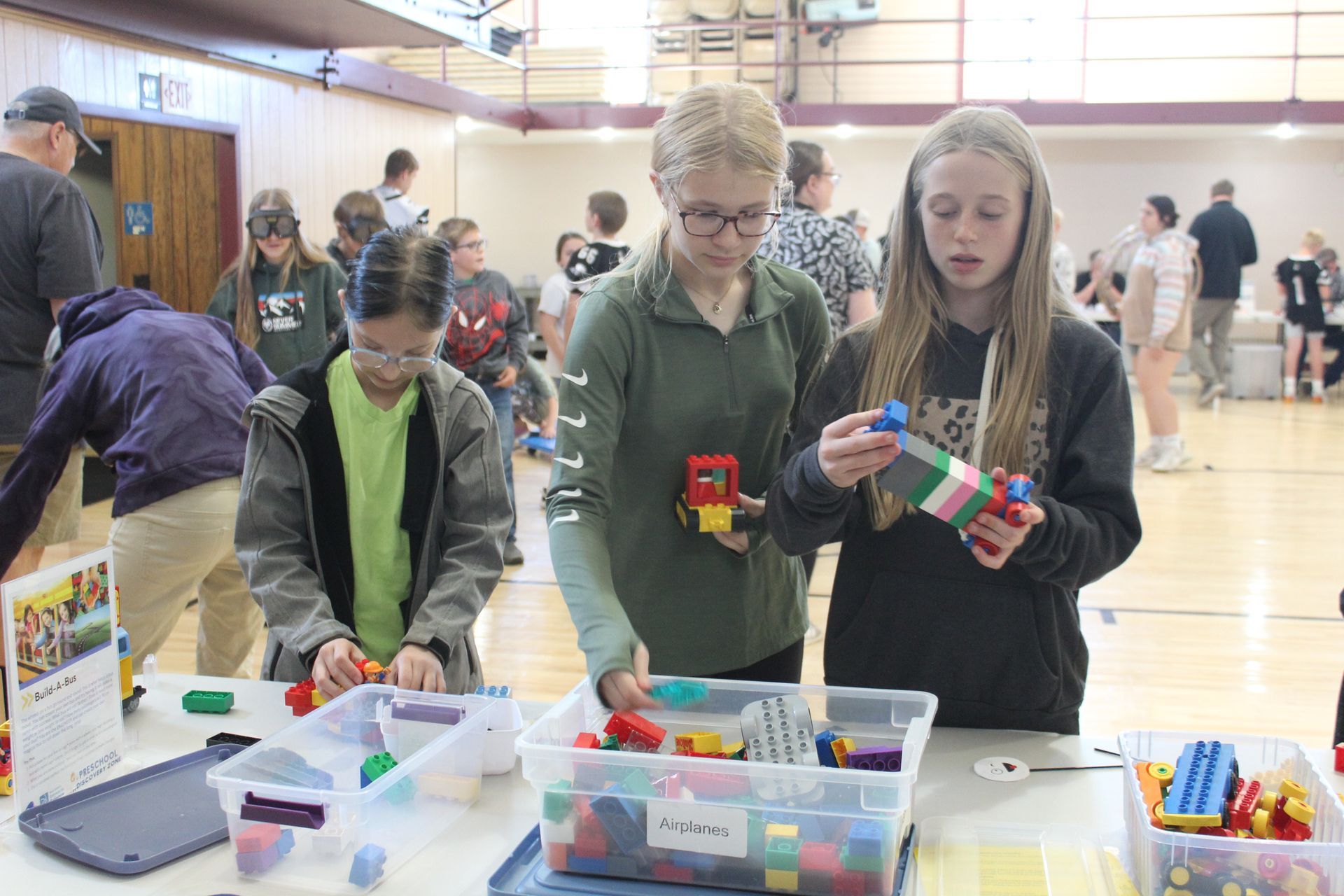 A group of young girls are standing around a table looking at lego blocks.
