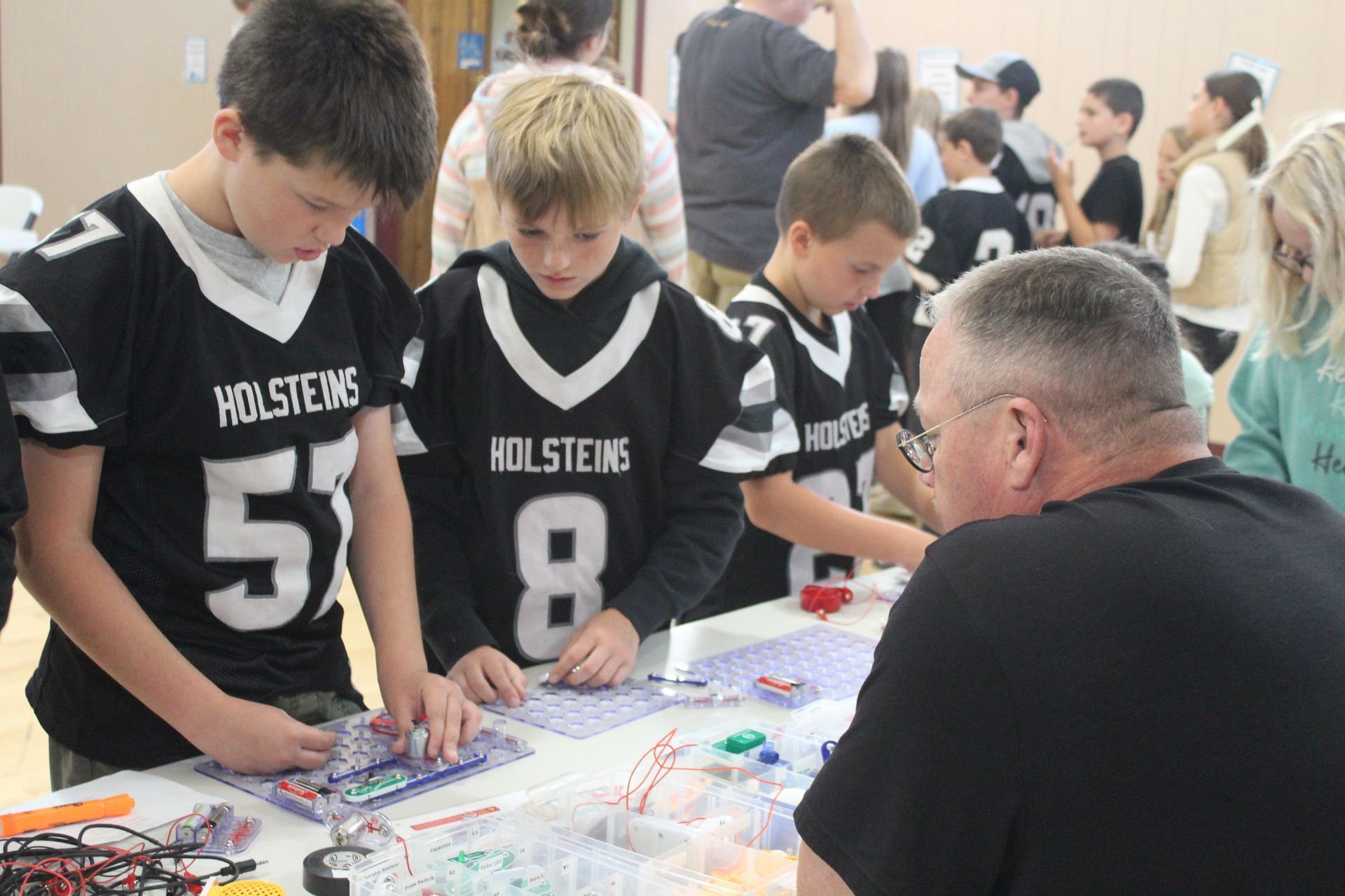 A group of young boys wearing holsteins jerseys are working on a project.