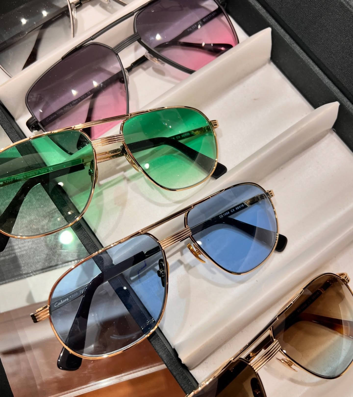 Un primo piano di quattro paia di occhiali da sole stile aviatore con lenti sfumate colorate, esposti su un vassoio.