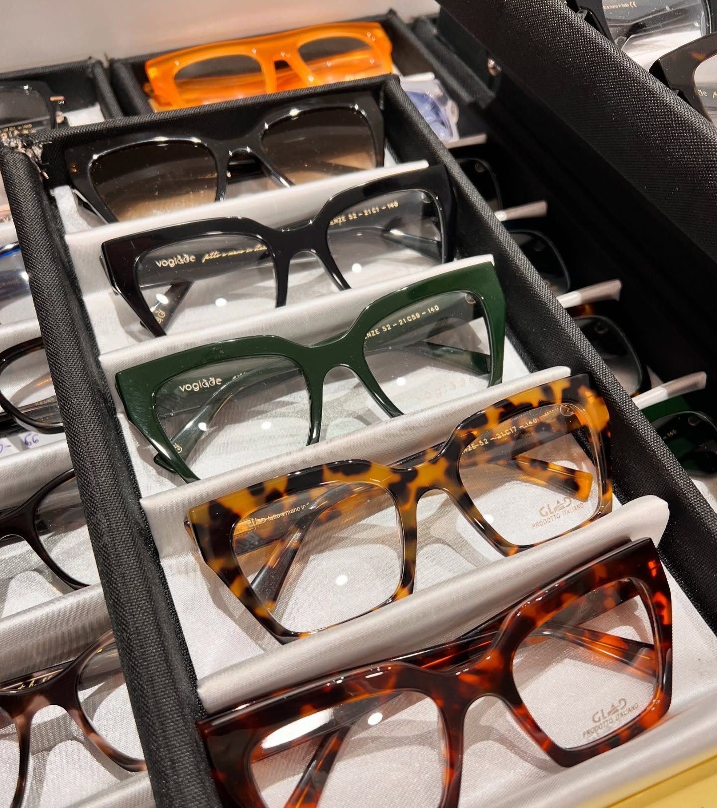 Un vassoio espositivo che contiene diverse paia di occhiali di vari colori e fantasie, tra cui nero, verde e tartaruga.
