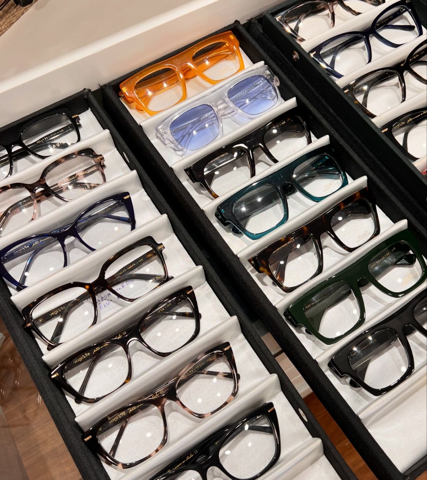 Un primo piano di diverse paia di occhiali di vari colori e stili, disposti su un vassoio espositivo nero.