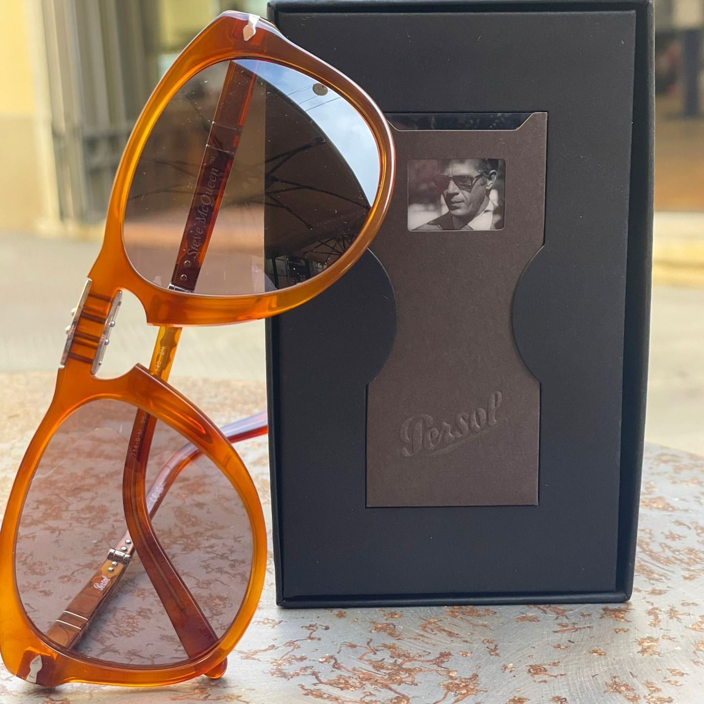 Occhiali da sole Persol con montatura color miele appoggiati davanti alla loro confezione regalo nera con il logo del marchio.