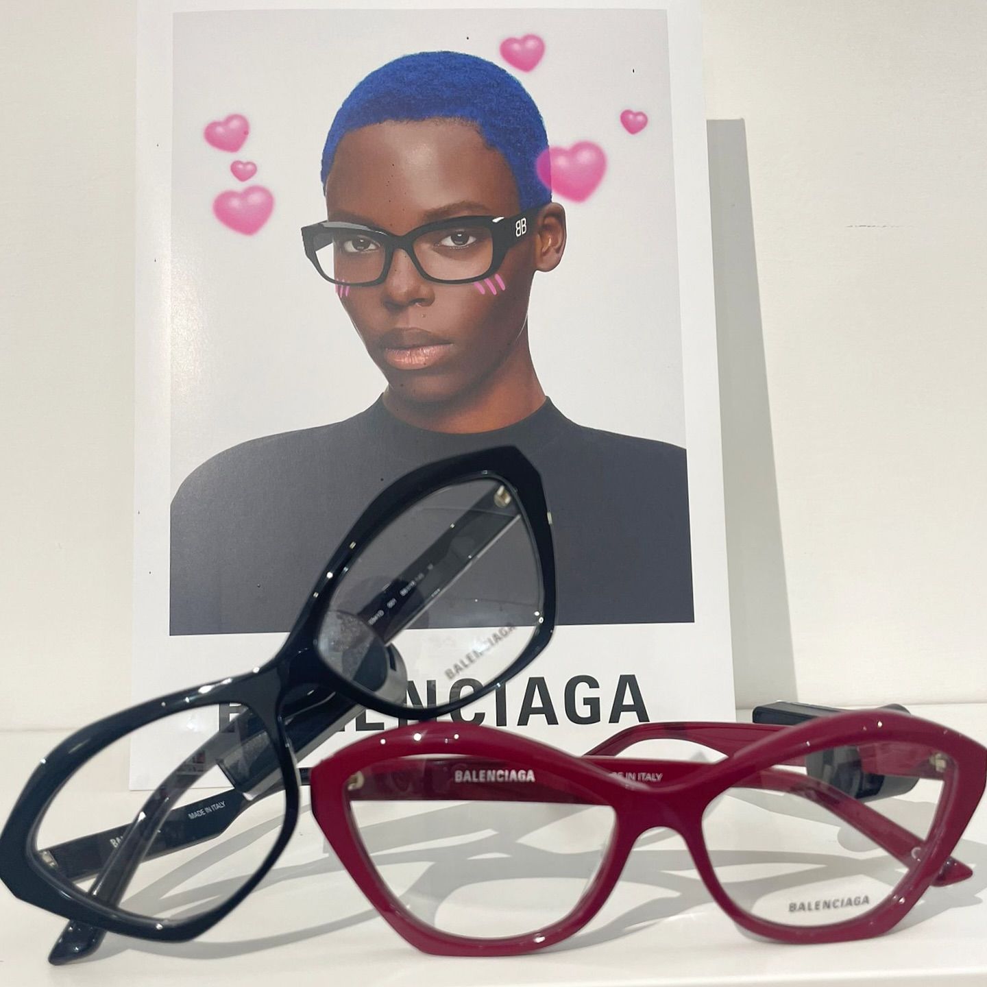 Una pubblicità di Balenciaga con occhiali da sole a occhi di gatto neri e bordeaux su uno sfondo bianco.