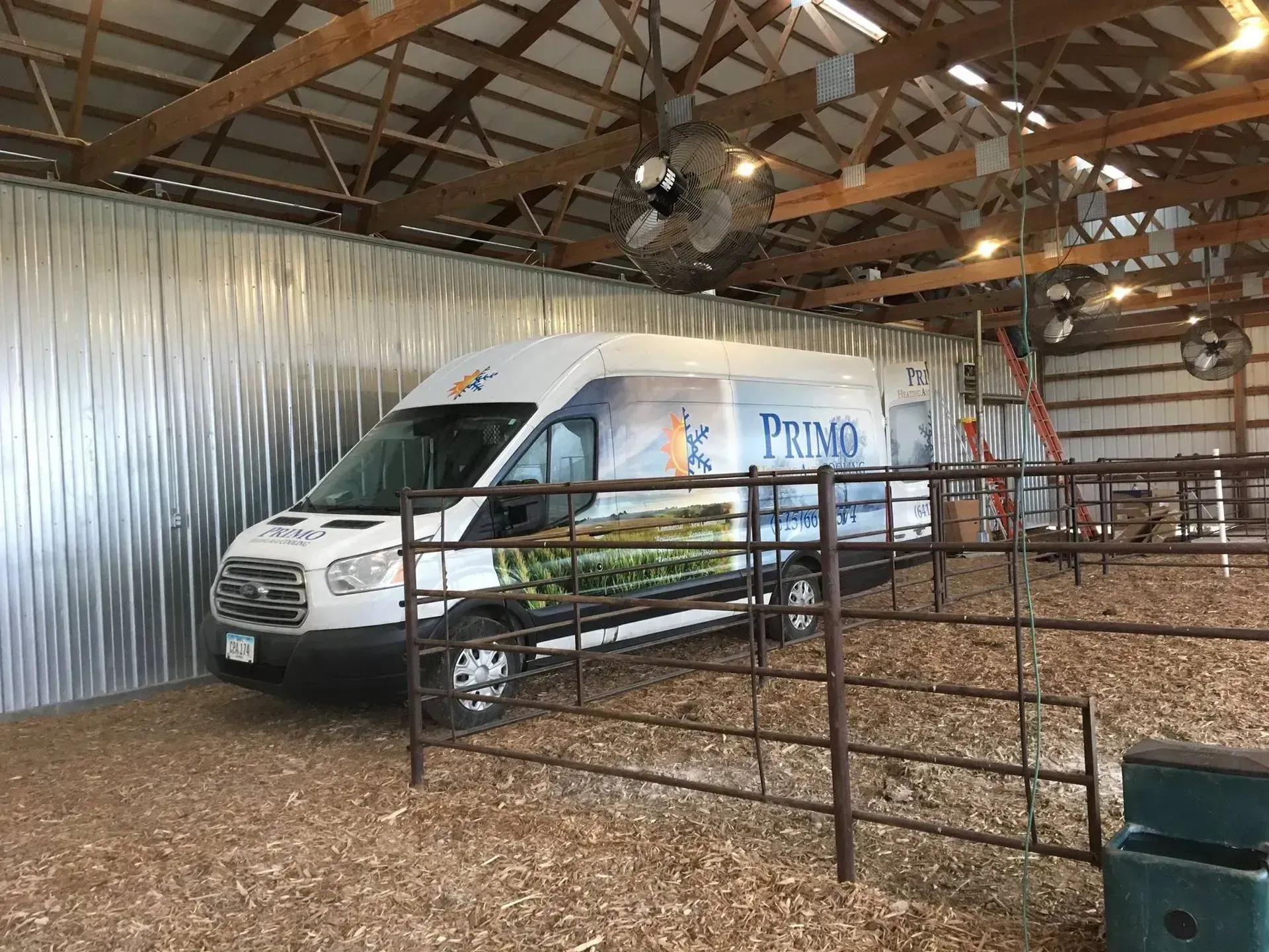 White van with a Prima logo parked inside a barn-like structure, metal walls, wooden beams, and a metal fence.