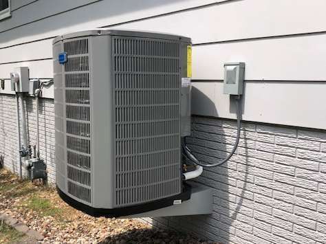 Air conditioner unit mounted on a wall, with electrical box and gas meter nearby.