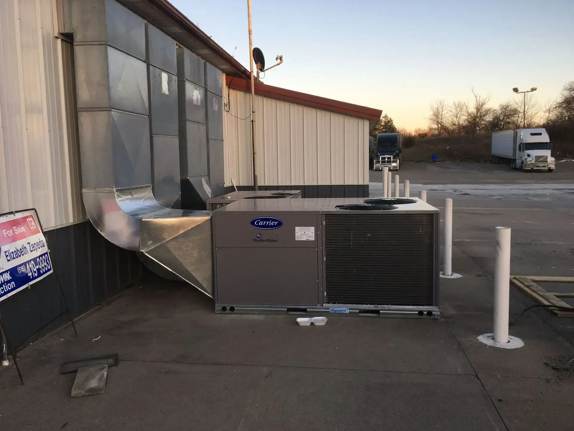 Exterior shot of a Carrier HVAC unit with ductwork attached to a building, next to a parking lot.
