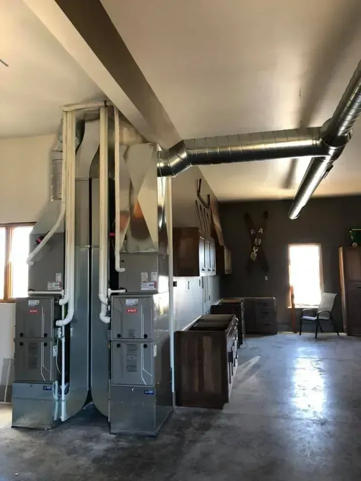 Heating and cooling system with large silver ducts and units in a room with light-colored walls and dark accent wall.