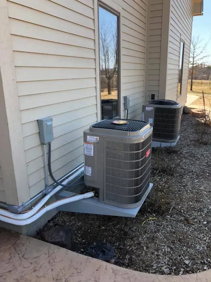 Two air conditioning units mounted outside a building, on concrete pads, near a window.