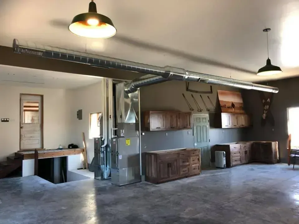 Spacious room with concrete floor, cabinets, HVAC unit, and ductwork. Two pendant lights hang from the ceiling.