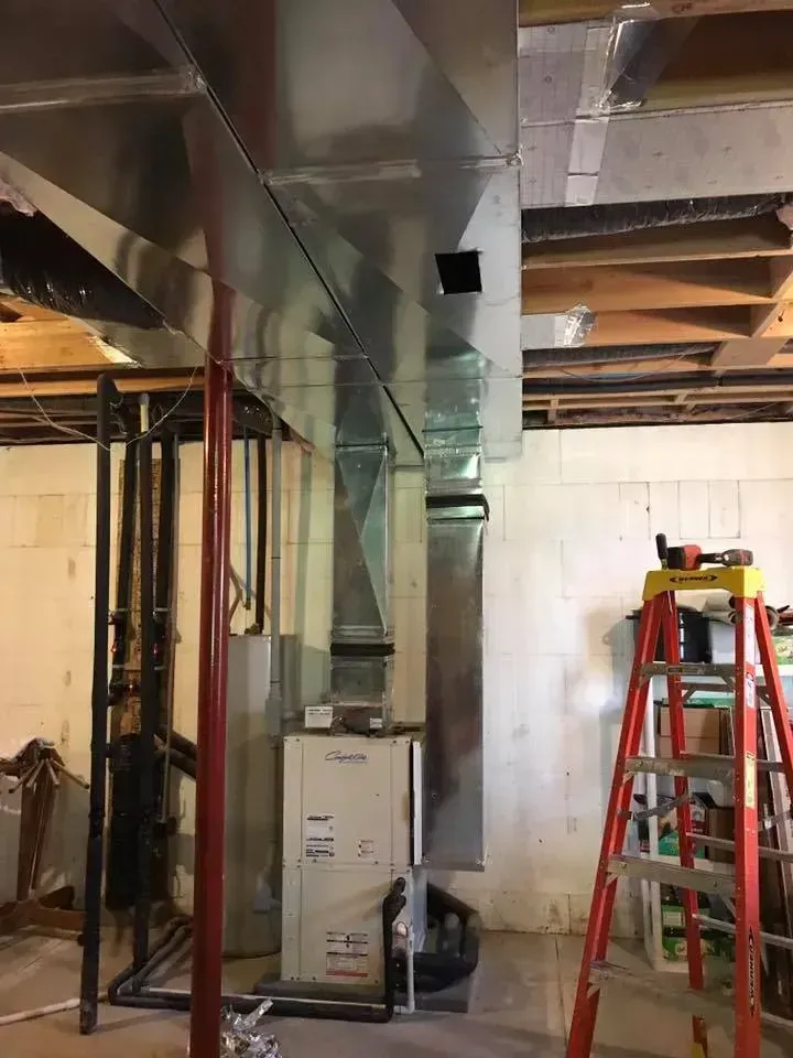 Furnace and ductwork in basement, with a ladder and exposed framing.