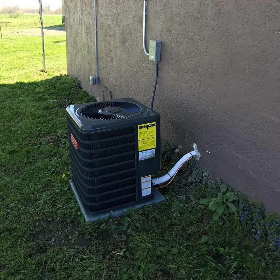 Air conditioning unit outside a building, on a concrete base, with electrical wiring.