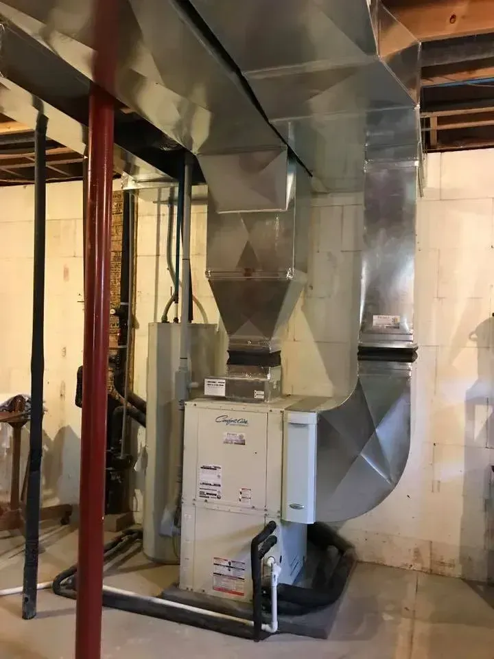 Furnace and ductwork in a basement setting; silver metal and white appliance.