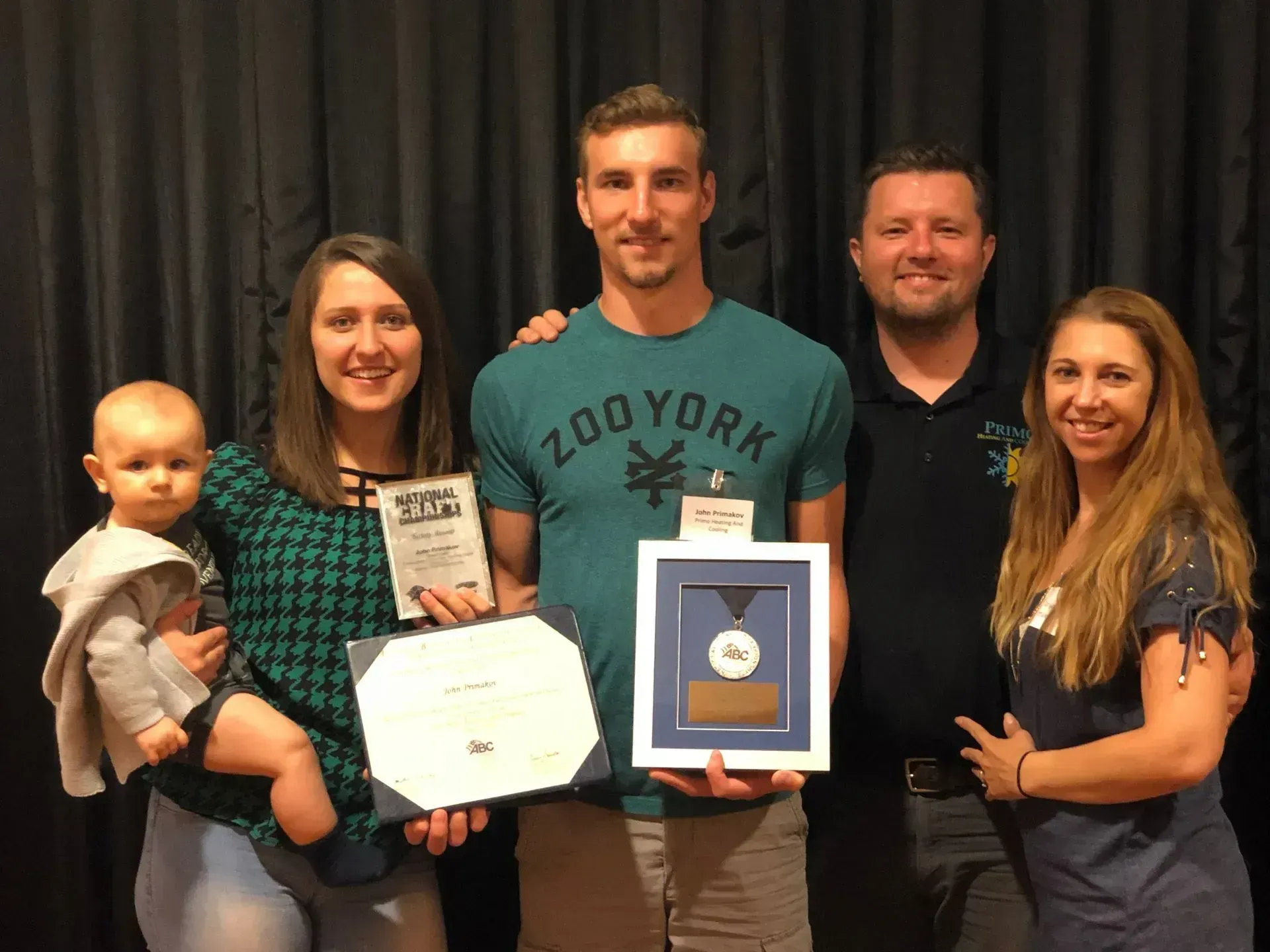 Group of five people holding awards, smiling, standing in front of a dark backdrop.